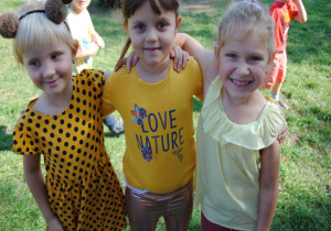 trzy uśmiechnięte dziewczynki ubrane w żółte kolory ubrań stoją w ogrodzie